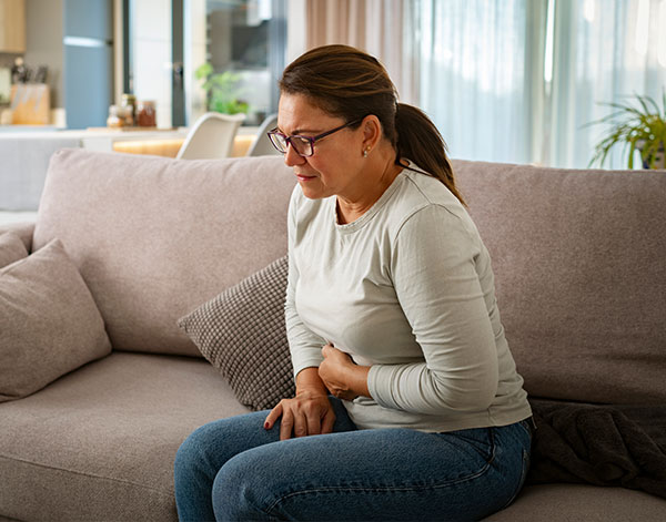 Unhealthy mature woman with stomachache sitting on the couch stock photo